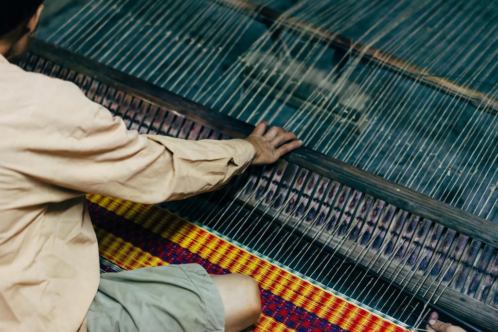 A person is weaving on a loom with a basket